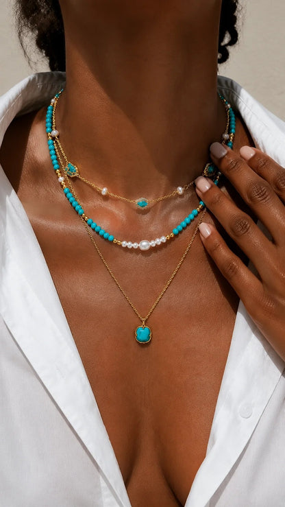 Close-up of a sun-kissed woman's décolletage showcasing a vibrant layered gold-tone necklace featuring turquoise stones and pearl accents.