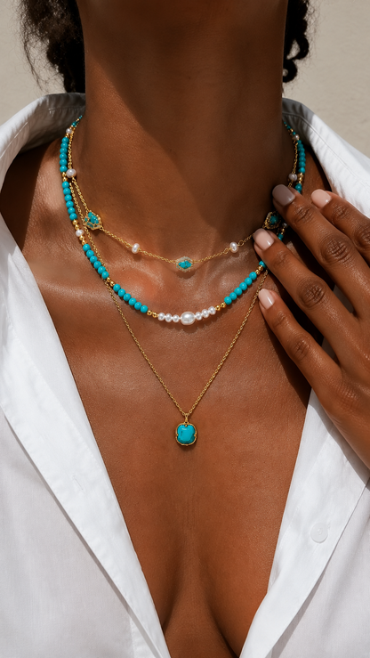 Close-up of a sun-kissed woman's décolletage showcasing a vibrant layered gold-tone necklace featuring turquoise stones and pearl accents.