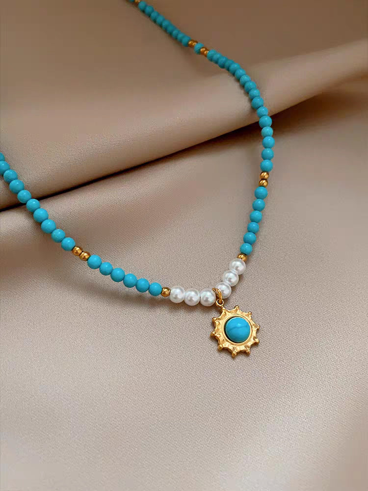 Detailed close-up of gold sunburst medallion pendant with central turquoise stone and surrounding pearls
