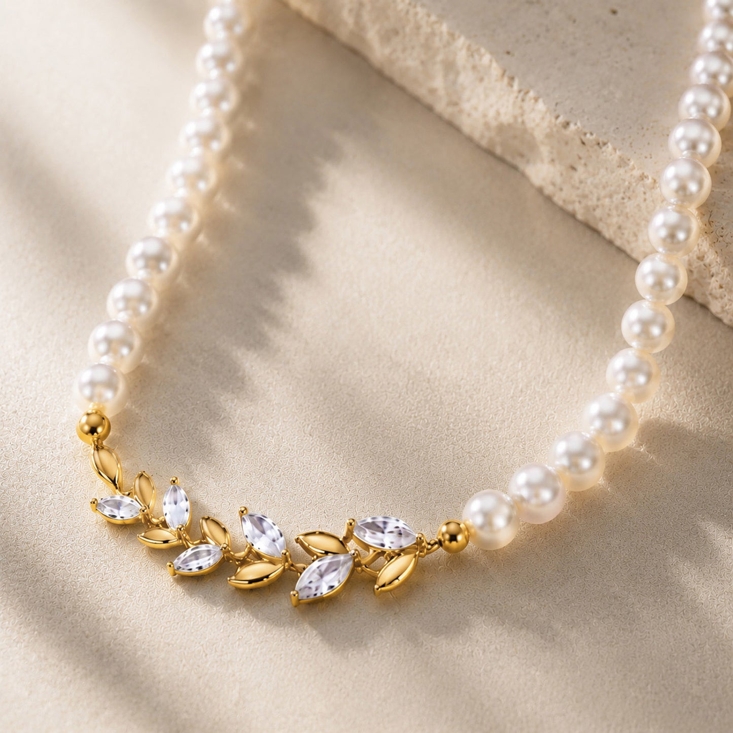 Macro close-up of a vintage 18K gold-plated pearl choker featuring a detailed micro-paved zircon laurel leaf centerpiece, resting gracefully on an aesthetic stone surface.
