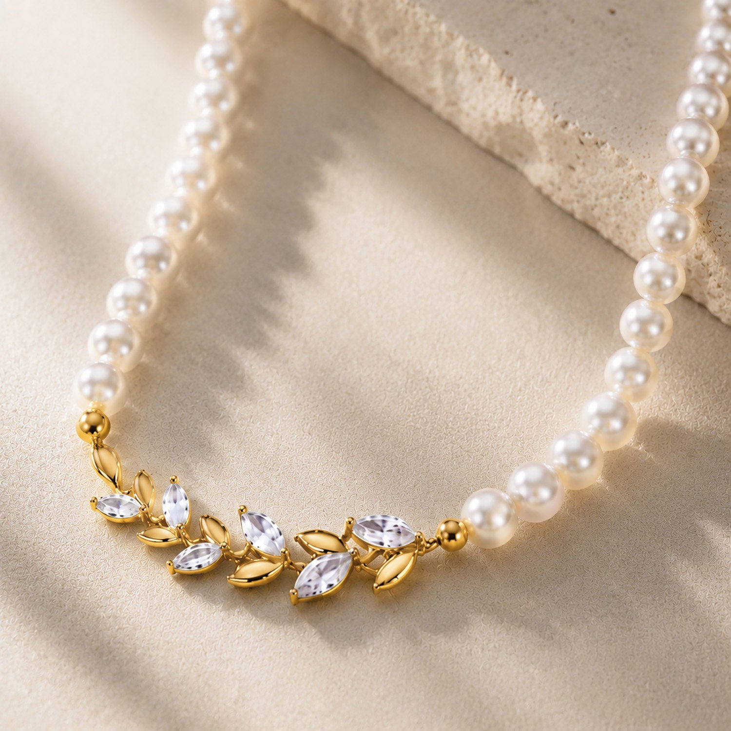 Macro close-up of a vintage 18K gold-plated pearl choker featuring a detailed micro-paved zircon laurel leaf centerpiece, resting gracefully on an aesthetic stone surface.