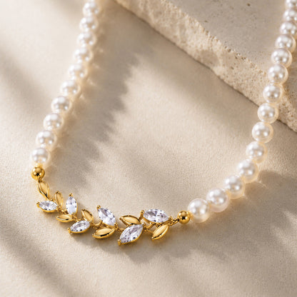 Macro close-up of a vintage 18K gold-plated pearl choker featuring a detailed micro-paved zircon laurel leaf centerpiece, resting gracefully on an aesthetic stone surface.