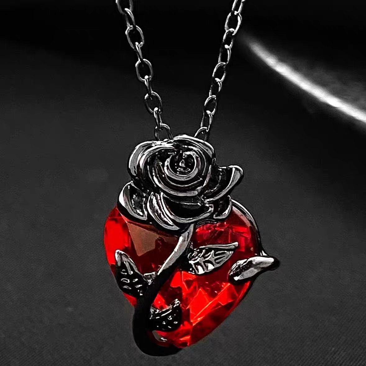 Close-up view of gothic black metal rose wrapped around a faceted red crystal heart pendant on dark background