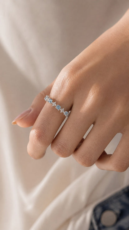 Close-up of model hand showcasing delicate aquamarine blue cz floral adjustable ring under warm natural sunlight
