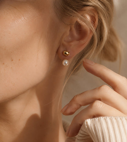 Macro close-up of a woman gently touching her elegant gold bean and pearl drop earring.