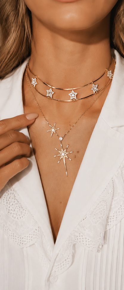 Close-up of an elegant woman's décolletage showcasing a sparkling gold-tone layered star necklace set against a white blouse.