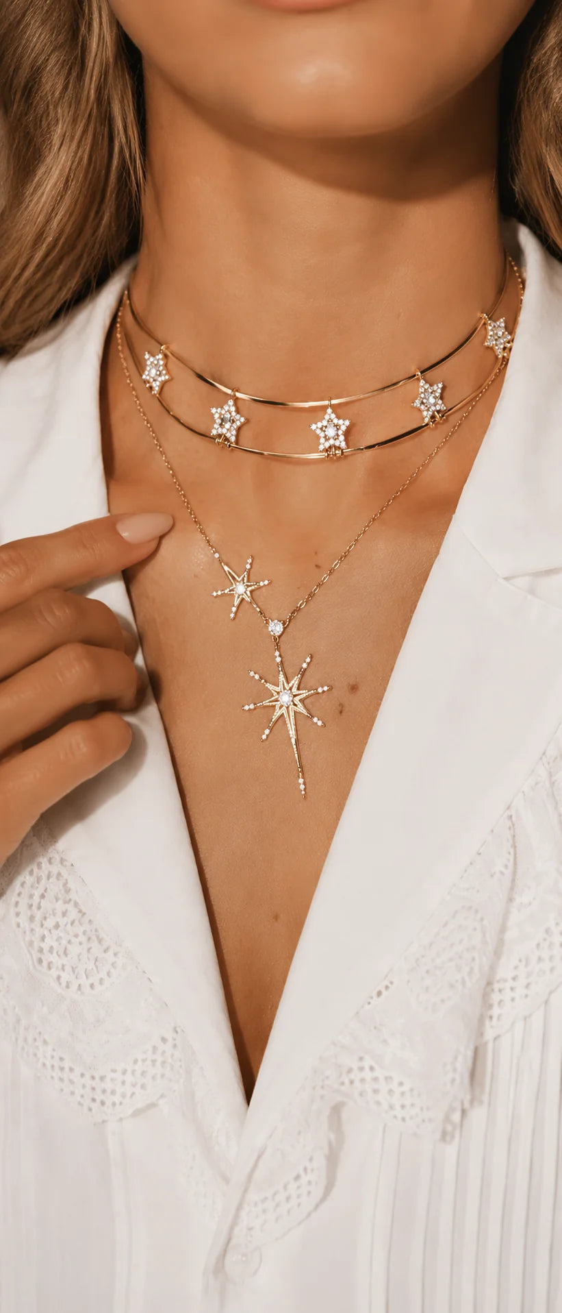 Close-up of an elegant woman's décolletage showcasing a sparkling gold-tone layered star necklace set against a white blouse.
