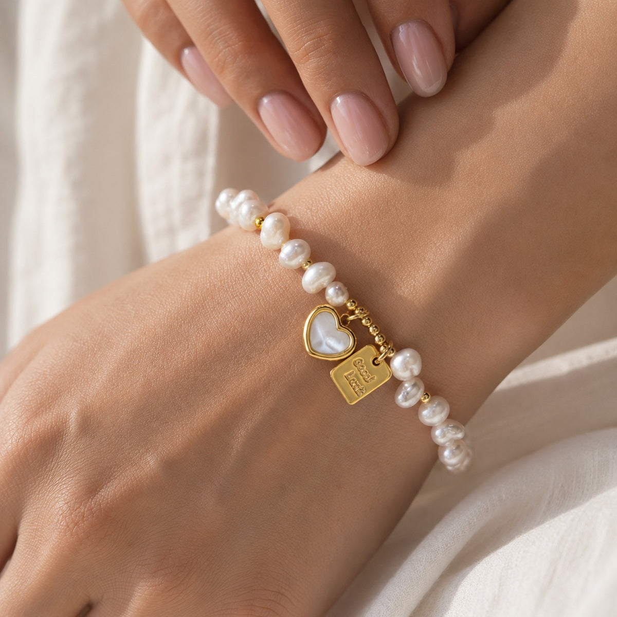 Close-up of model's wrist displaying freshwater pearl beaded bracelet with gold good luck tag charm