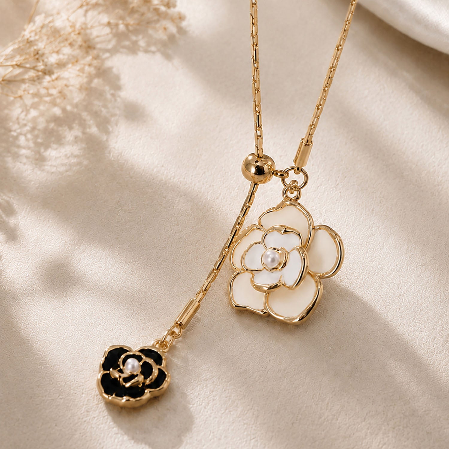 Close-up detail of a vintage gold-tone Y-necklace featuring intricate white and black camellia flower pendants with pearl accents, resting on a warm aesthetic surface.