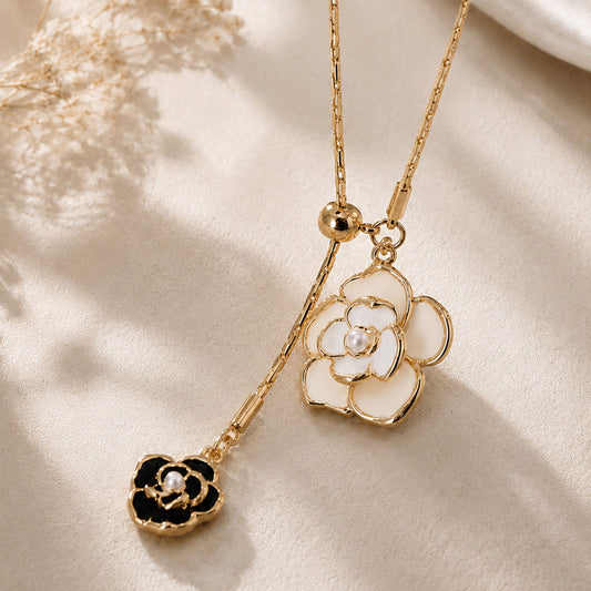 Close-up detail of a vintage gold-tone Y-necklace featuring intricate white and black camellia flower pendants with pearl accents, resting on a warm aesthetic surface.