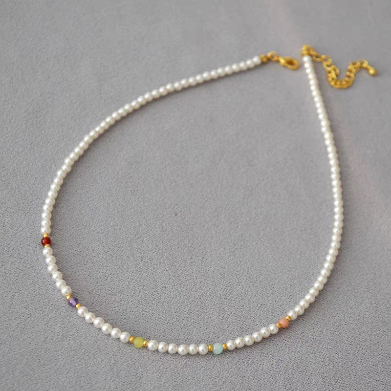 Flat lay of colorful beaded pearl choker necklace with gold-plated lobster clasp and extender chain on gray fabric