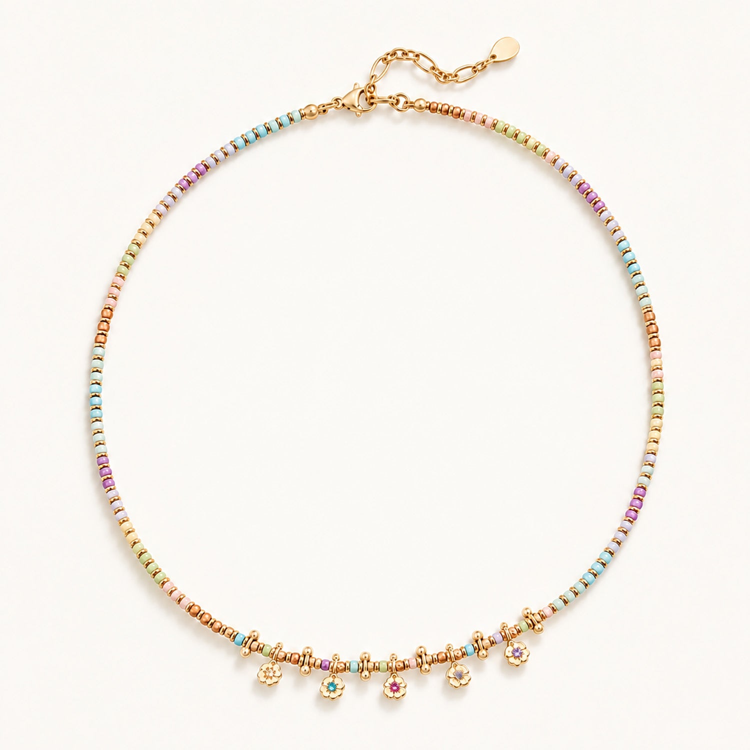 Minimalist flat lay of a gold-tone beaded necklace featuring natural stones and dainty floral pendants.