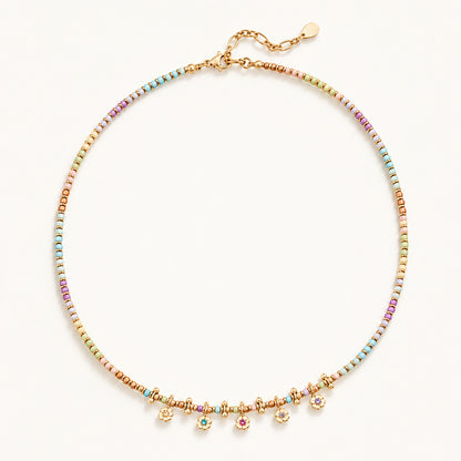 Minimalist flat lay of a gold-tone beaded necklace featuring natural stones and dainty floral pendants.