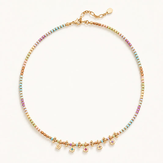 Minimalist flat lay of a gold-tone beaded necklace featuring natural stones and dainty floral pendants.