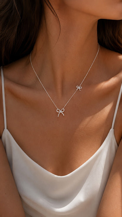 Close-up of a model wearing a dainty S925 sterling silver double bow necklace paired with a white silk camisole.