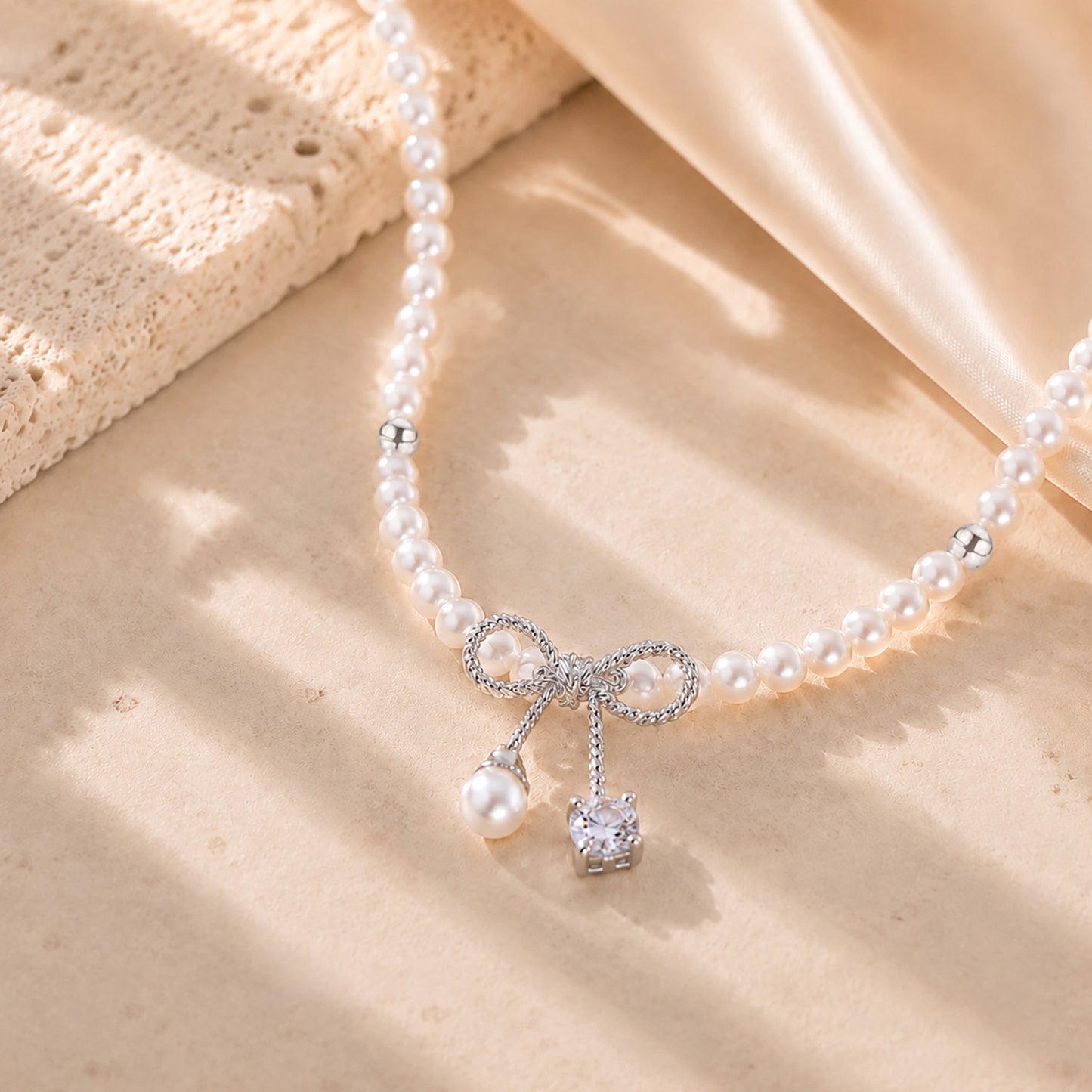 Close up of a delicate white gold-tone bowknot pendant with a pearl and sparkling zirconia drop.