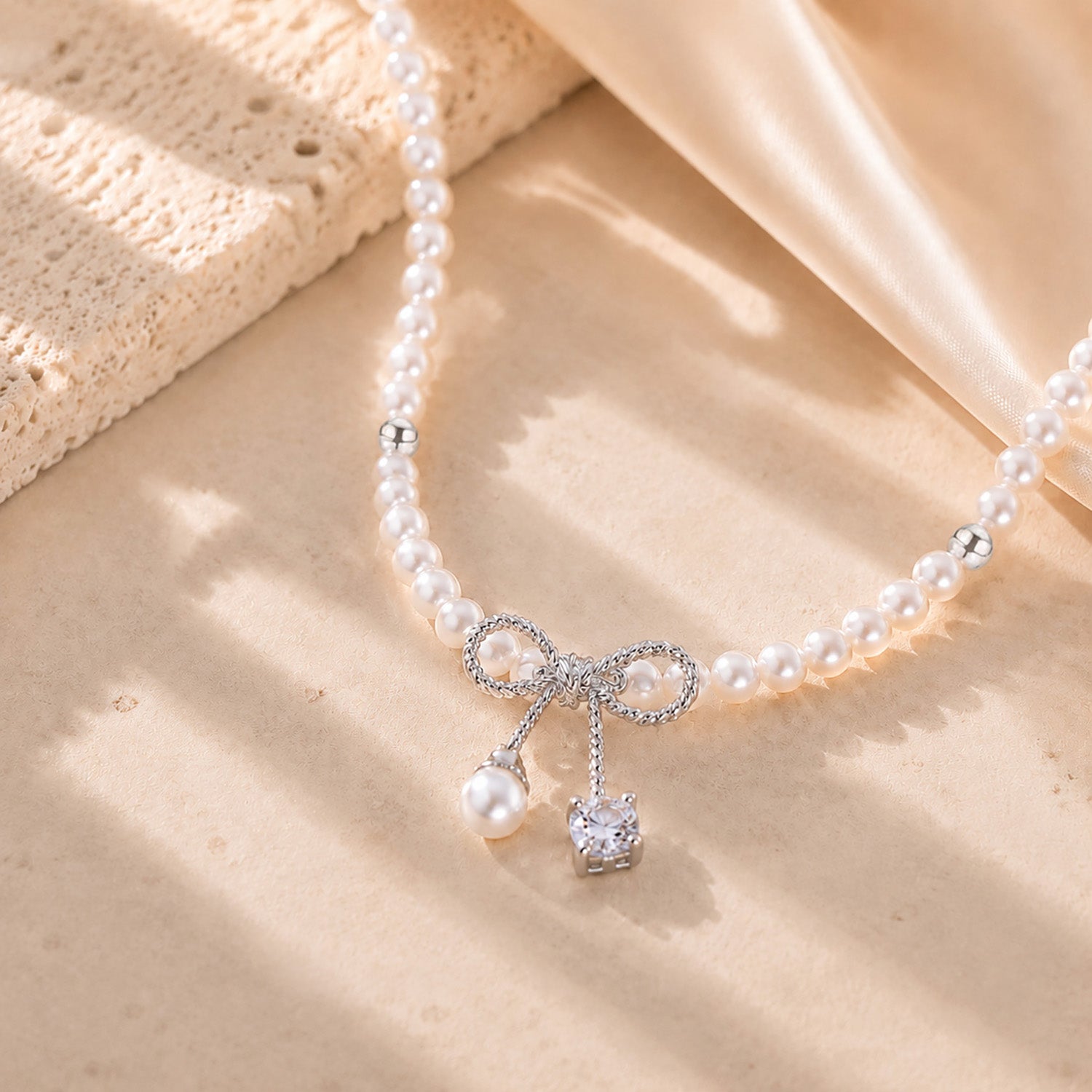Close up of a delicate white gold-tone bowknot pendant with a pearl and sparkling zirconia drop.
