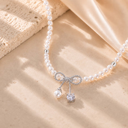 Close up of a delicate white gold-tone bowknot pendant with a pearl and sparkling zirconia drop.