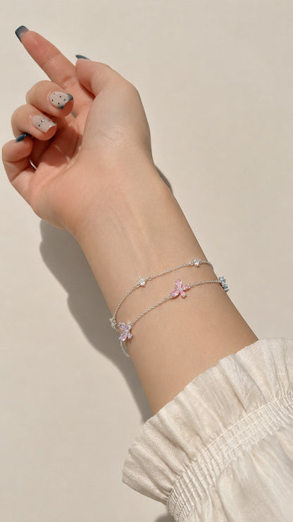 Model wrist detail showing layered silver chain bracelet with pink blue crystal flower accents