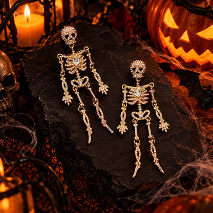 Gold rhinestone skeleton dangle earrings displayed on black stone with Halloween pumpkin background