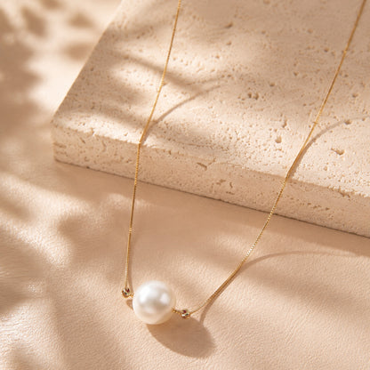 Elegant single pearl pendant necklace with a gold-tone chain laid on textured stone and silk.
