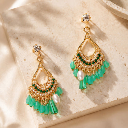 Close up of intricate gold-tone bohemian dangle earrings with green crystals resting on a warm stone surface.