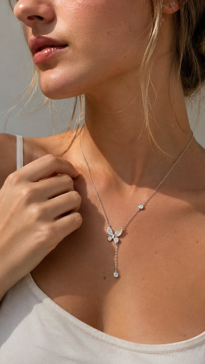 Close-up of a blonde model wearing a silver butterfly lariat Y-necklace with a white V-neck top under warm sunlight.