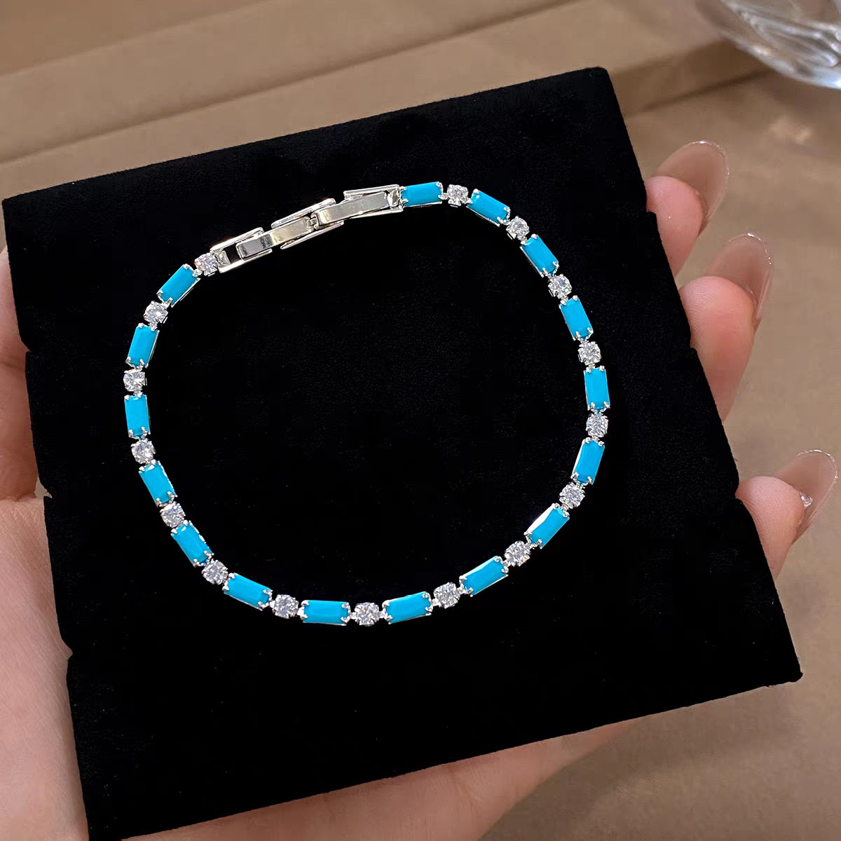 Flat lay of turquoise blue geometric CZ tennis bracelet displayed on black velvet pad showing fold-over clasp