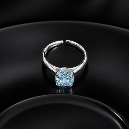 High-angle shot of silver adjustable ring with ice blue gemstone resting on black reflective dish