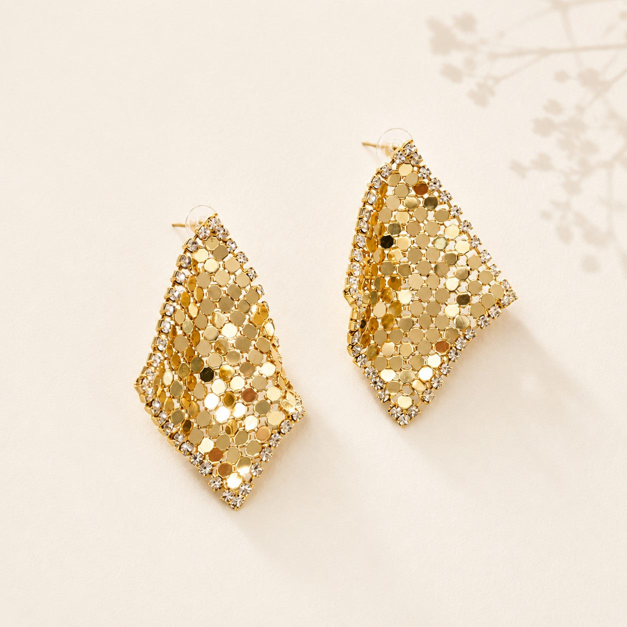 Flatlay view of pair of gold plated liquid metal mesh scarf rhombus stud earrings with pave CZ crystals
