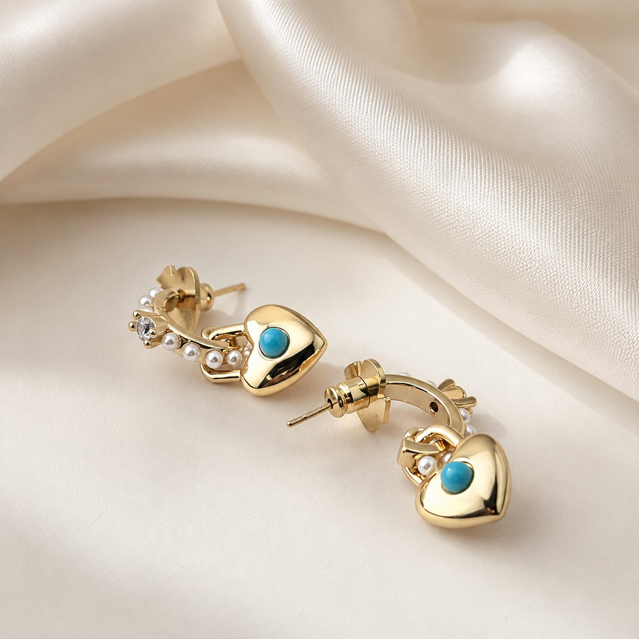 Side view showing the 3D thickness of gold turquoise heart padlock earrings resting on silk fabric
