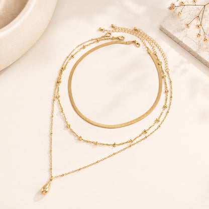 Gold layered necklace set styled on travertine stone plate with dry flowers