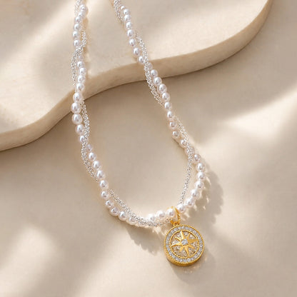 Macro detail of a sparkling zirconia eight-pointed star compass pendant attached to a twisted double-layer pearl and metal chain.