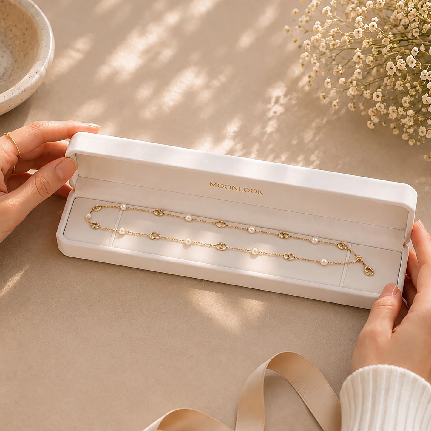 Hands displaying a delicate gold-tone pearl and anchor link lariat necklace inside a premium white Moonlook jewelry box.