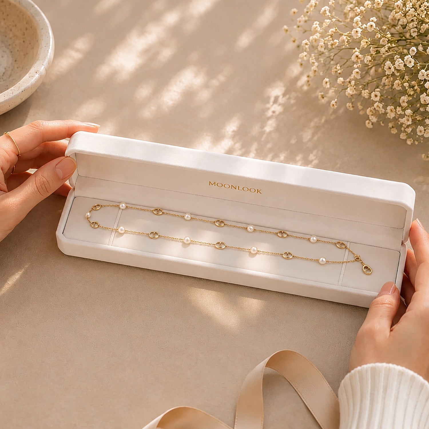 Hands displaying a delicate gold-tone pearl and anchor link lariat necklace inside a premium white Moonlook jewelry box.