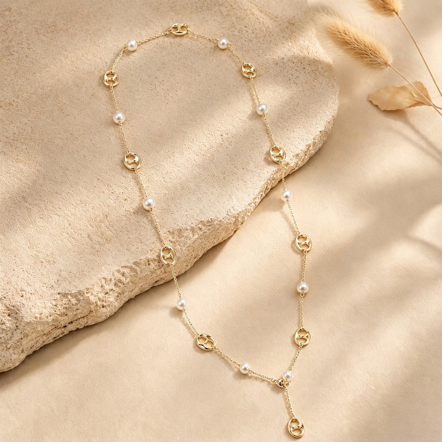 Gold-tone pearl and anchor chain long necklace draped elegantly over a textured stone surface.