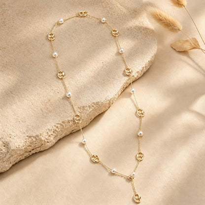 Gold-tone pearl and anchor chain long necklace draped elegantly over a textured stone surface.