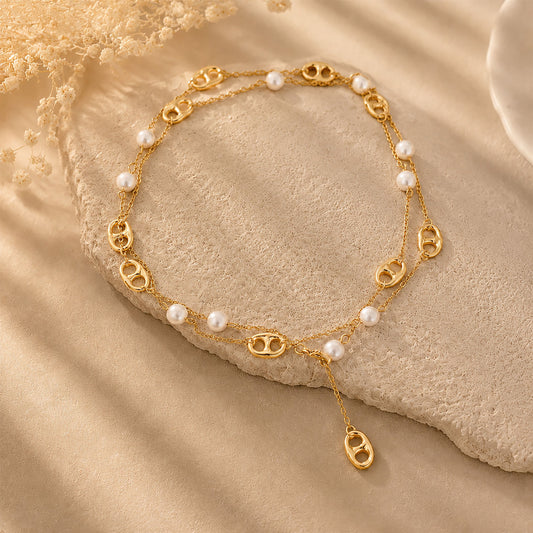 Versatile gold-tone pearl and mariner chain necklace styled in a double layer on a warm textured stone background.