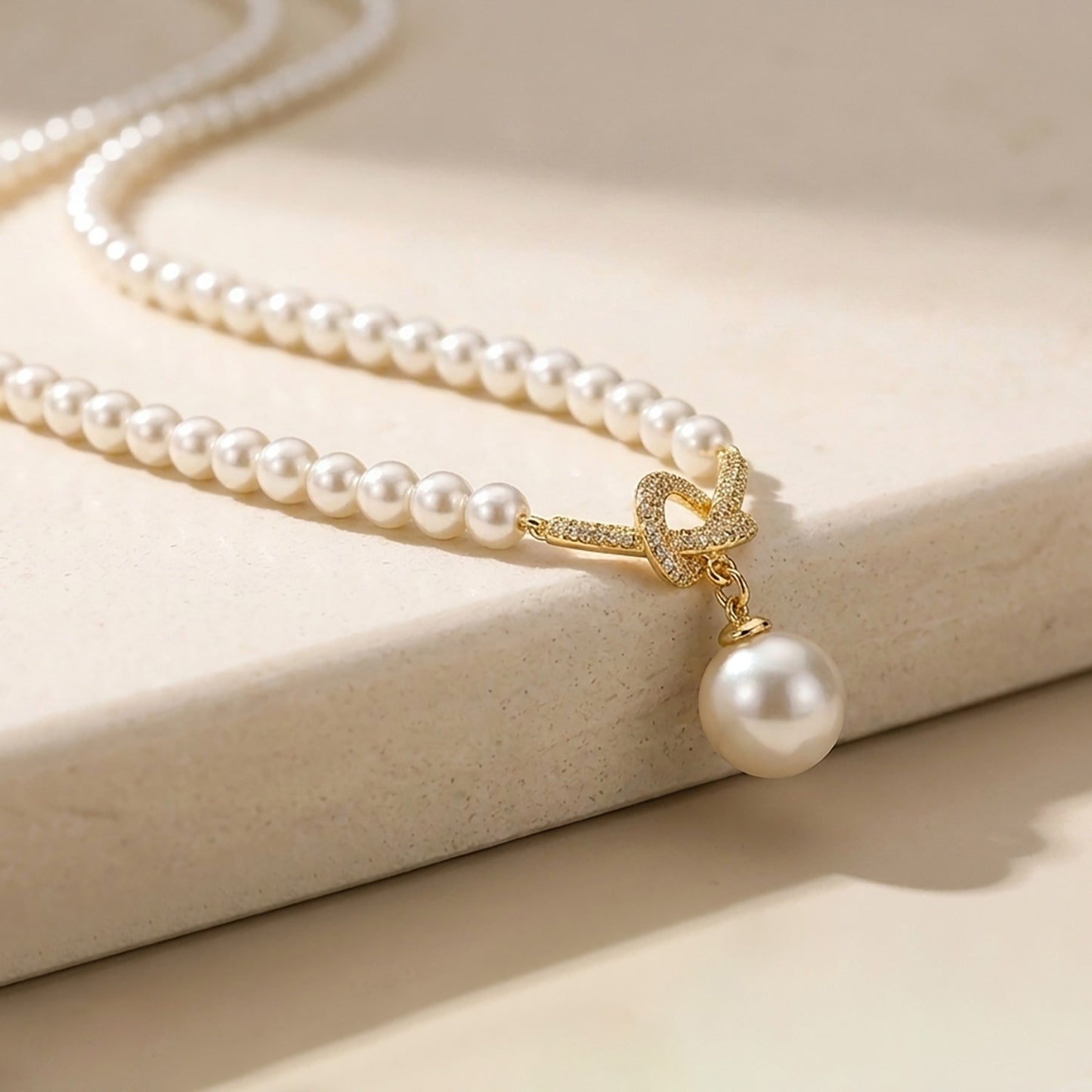 Macro detail of a sparkling 18K gold-tone twisted knot and lustrous pearl drop pendant.