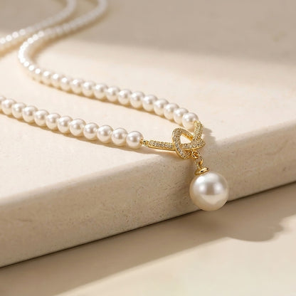 Macro detail of a sparkling 18K gold-tone twisted knot and lustrous pearl drop pendant.