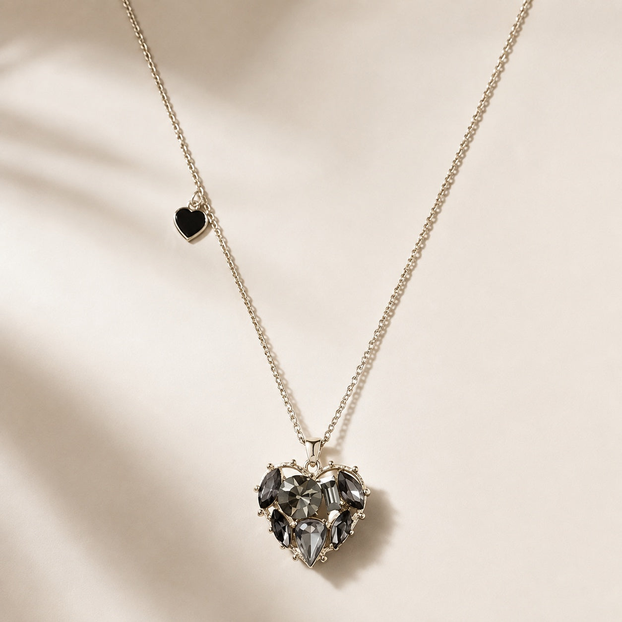 Flatlay view of black CZ crystal heart pendant necklace with silver chain and side mini heart charm