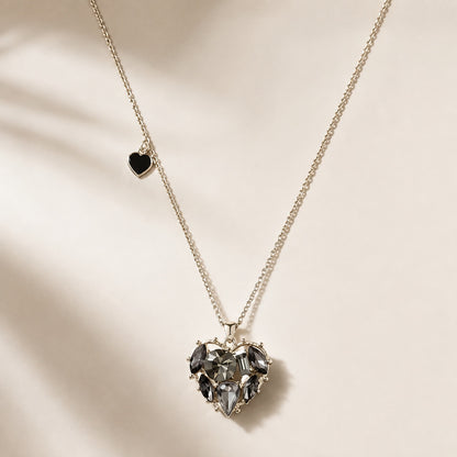 Flatlay view of black CZ crystal heart pendant necklace with silver chain and side mini heart charm