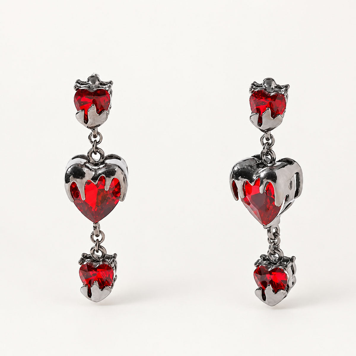 Pair of gothic bleeding red heart drop earrings encased in gunmetal molten metal on white background