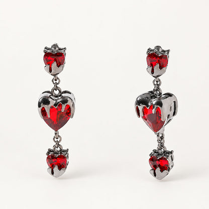 Pair of gothic bleeding red heart drop earrings encased in gunmetal molten metal on white background