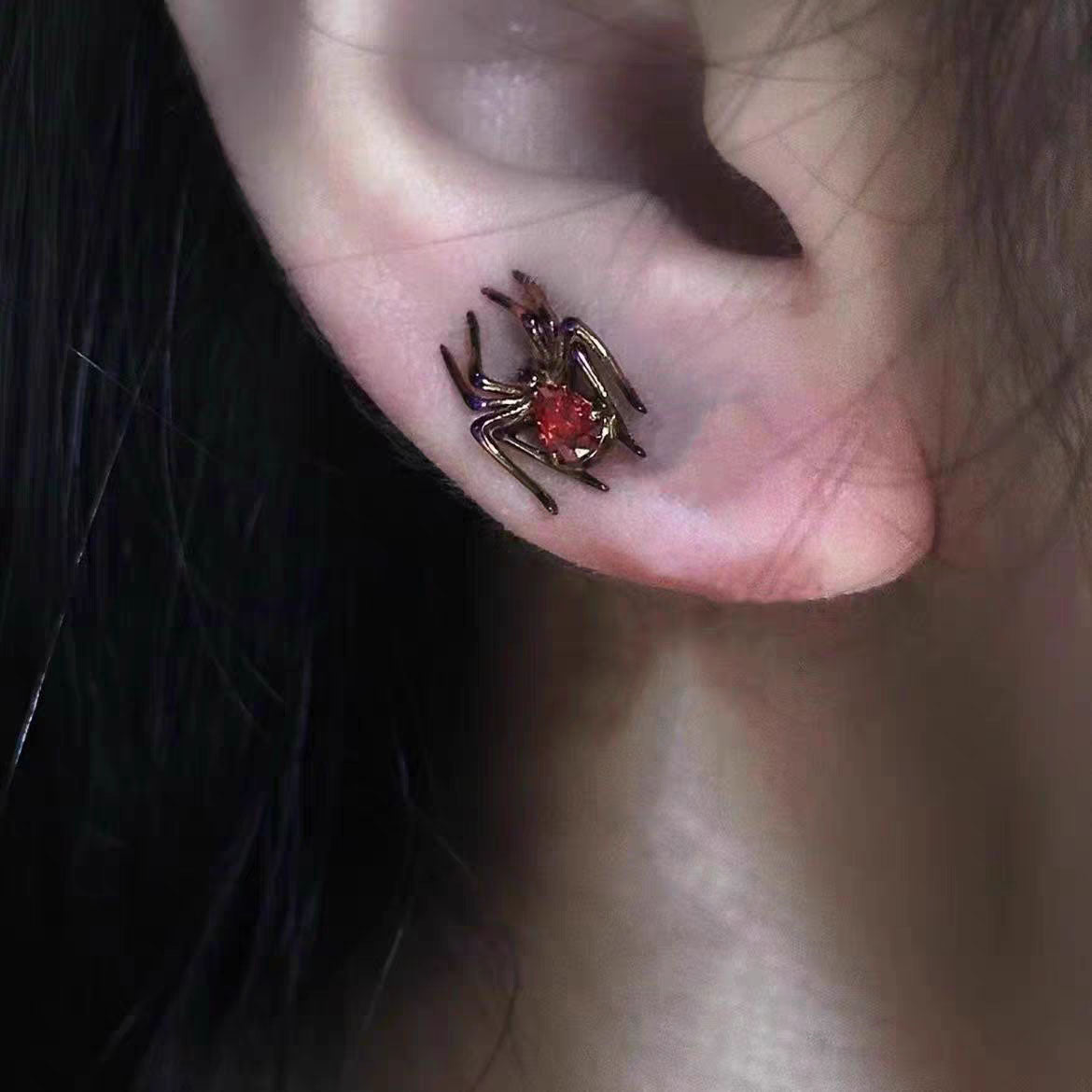 Model wearing gothic dark gunmetal spider stud earring with crimson red CZ crystal body