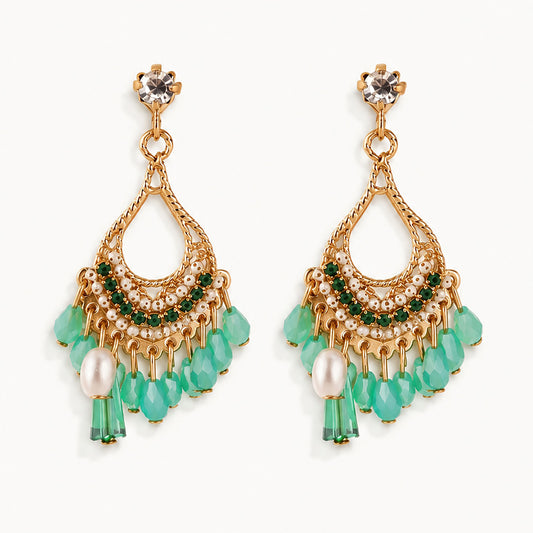 Detailed view of gold-tone teardrop earrings featuring emerald green crystal fringe and faux pearl accents on a white background.