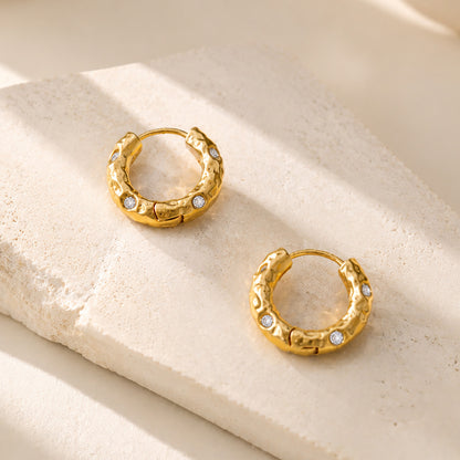 Close-up of 16mm vintage-inspired hammered gold-tone hoop earrings adorned with subtle zirconia accents resting on an aesthetic stone block.