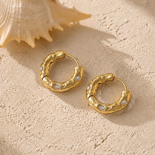 Artistic flat lay of textured gold-tone hoop earrings next to a natural seashell, highlighting their organic, coastal-inspired aesthetic.