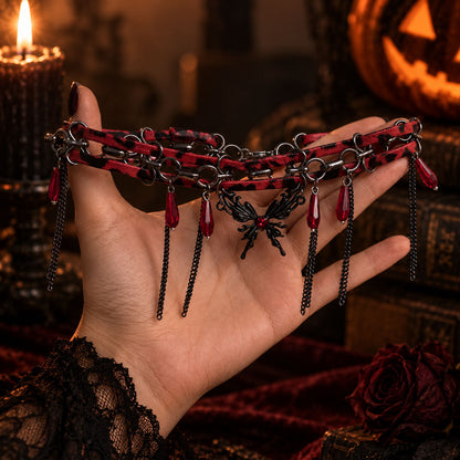 Hand holding gothic red-and-black leather butterfly chain choker with dangling red acrylic teardrops