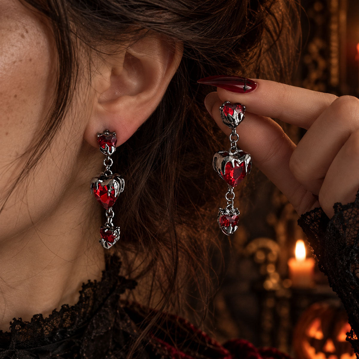Hand adjusting gothic triple-tiered red heart crystal drop earrings on model ear